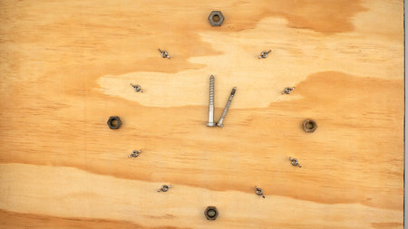 Creative concept of a clock made of bolts, wing nuts and screws. Timber background with copy space.