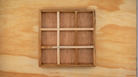 A wooden box with empty compartments, suitable for creating a concept or a board game of noughts and...