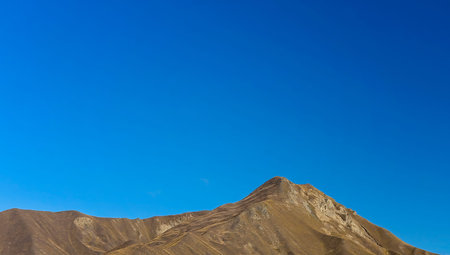 A bare brown mountain range against a clear blue sky