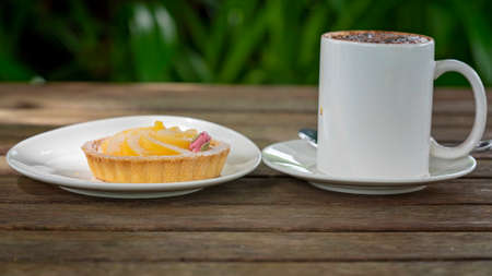 Cappuccino coffee with a lemon citrus tart on and outdoor timber tableの写真素材