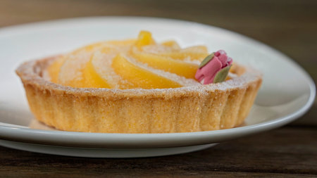 Close up of a lemon citrus tart with rose icing decoration presented on a white plate