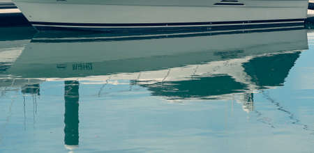 Close up of the sleek hull of a boat on the waterline reflected in the waterの写真素材
