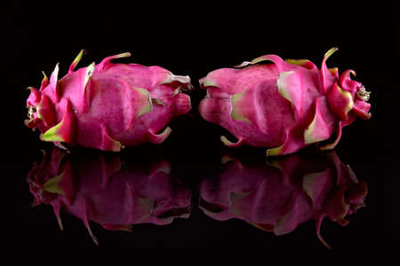 Two dragon fruit placed on the edge of a black tank of water to catch the reflectionsの写真素材