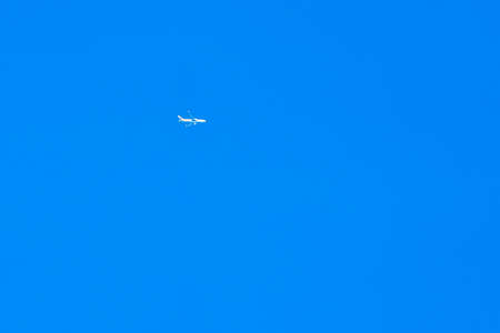 An white aeroplane flying high in a clear blue skyの写真素材