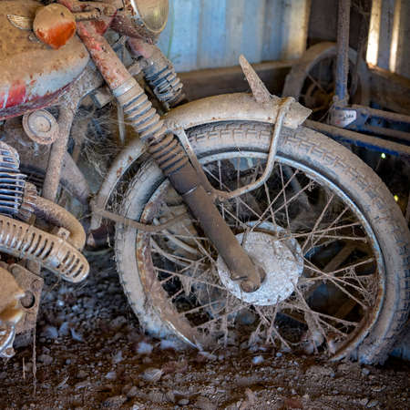 Closeup of the front wheel of a rusted vintage motorcycle covered in dirt and cobwebsの写真素材