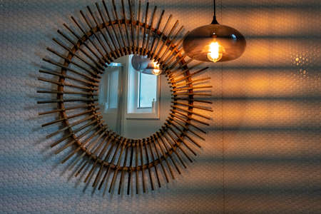 Hanging light casting a soft glow on a decorative bathroom mirror on a tiled wallの写真素材