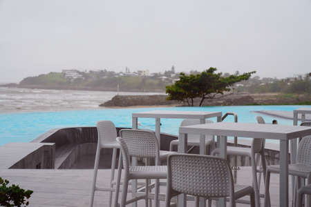 Cafe tables and chairs beside an infinity pool by the ocean on a wet and windy grey overcast dayの写真素材