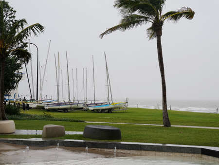 Small sailing yachts on trailers parked on grass beside the ocean on a wet and windy dayの写真素材