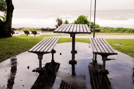 Timber table and stools for outdoor beachfront dining with an ocean view on a wet and rainy dayの写真素材