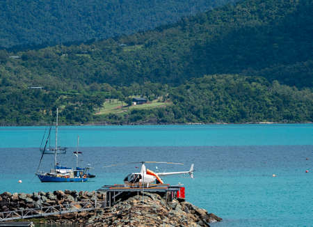 Airlie Beach, Queensland, Australia - April 2021: Passengers board a helicopter on an oceanfront helipad with boats in the backgroundのeditorial素材