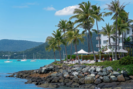 Airlie Beach, Queensland, Australia - April 2021: Holidaymakers relaxing at oceanfront hotel resort with rocky shore and yachts at anchorのeditorial素材