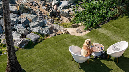 Airlie Beach, Queensland, Australia - April 2021: Woman sunbathing and reading phone in a chair on holiday at a hotel resortのeditorial素材