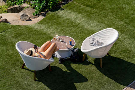 Airlie Beach, Queensland, Australia - April 2021: Woman sunbathing and reading phone in a chair on holiday at a hotel resortのeditorial素材