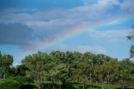 A colorful rainbow in the cloudy sky over the treed banks of a damの写真素材