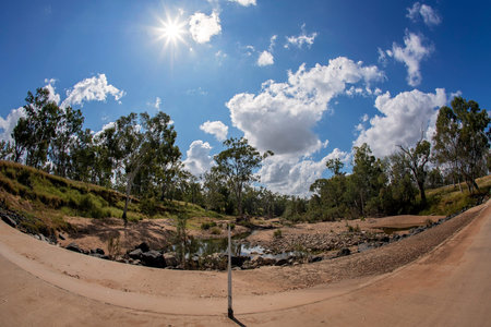 An almost dry outback country creek with rocky bed and guide post in center of road, sun flare,...
