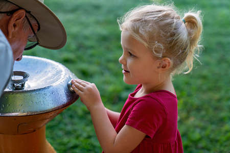 Mackay, Queensland, Australia - June 2021: Young girl child and her grandfather at a drinking fountain in the public botanic gardensのeditorial素材