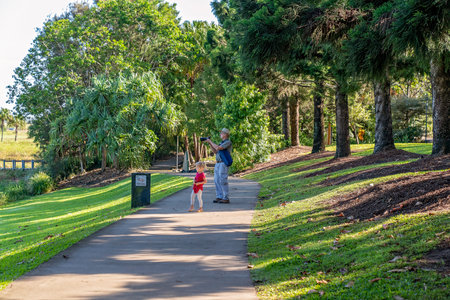 Mackay, Queensland, Australia - June 2021: A young child stands beside her grandfather as he takes a photo in the botanic gardensのeditorial素材