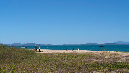 Cape Gloucester, Queensland, Australia - June 2021: Families playing on the sand at beachfront tropical resort with boats moored in the background on a summer dayのeditorial素材