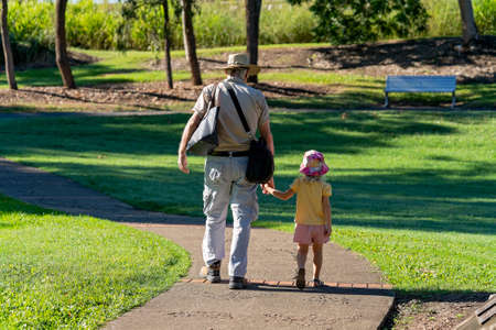 Mackay, Queensland, Australia - June 2021: A grandfather carrying bags holds his granddaughter's hand as they walk together in the botanic gardensのeditorial素材