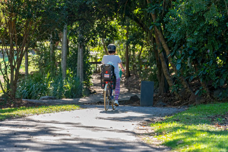 Mackay, Queensland, Australia - June 2021: A mother cycles on a bike in the botanic gardens with her young child strapped into the seat behind herのeditorial素材