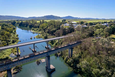 Aerial of empty sugar cane bins being pulled across a country creek by a train, parallel to a highway bridgeの写真素材