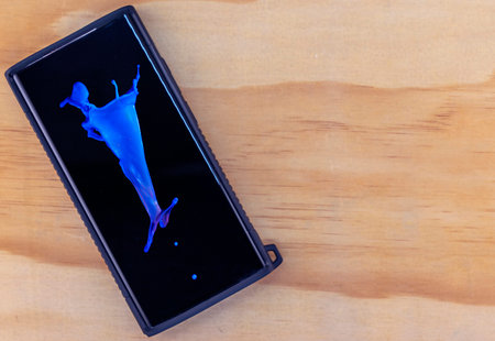 Mobile phone with blue waterdrop splash on screen on timber background with space for text