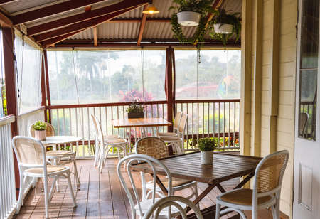 Cafe tables and chairs on a plastic enclosed timber verandah of historic houseの写真素材