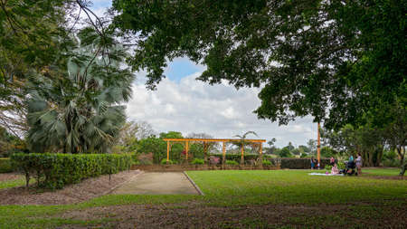 Mackay, Queensland, Australia - September 2021: Female friends having a picnic in the park with their small children beside an arch feature at botanic gardensのeditorial素材