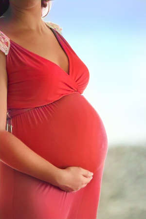 Pregnant woman in red dress soft focus to show shape of her bellyの写真素材