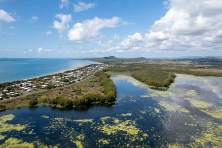 High perspective drone landscape of beachfront suburb backed by a natural lagoon covered with aquatic plants and banks of bushland with cloudy water reflections, Salonika Beach, Queensland, Australiaの写真素材