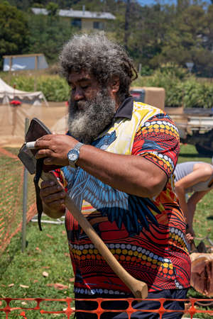 Eungella, Queensland, Australia - October 2021: A bearded aboriginal man wearing a watch and colorful shirt wielding an ax at a country re-enactment fairのeditorial素材