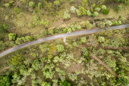 Drone aerial view down onto a car parked beside a country road amongst bushlandの写真素材