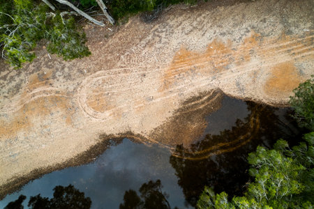 Top down aerial of vehicle tracks in the sand on the banks of a shallow country creek