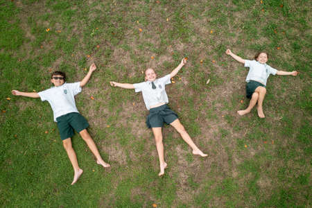 Townsville, Queensland, Australia - November 2021: Three children in school uniforms lying on the grass under a drone as it comes in to landのeditorial素材