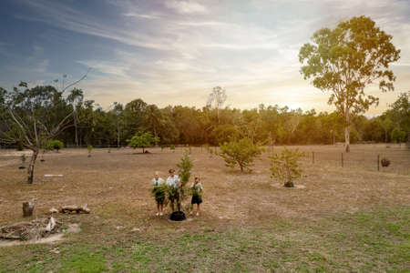 Townsville, Queensland, Australia - November 2021: Three school aged children hiding behind a tree as a drone comes towards them to take a photograph in late afternoon sunlightのeditorial素材
