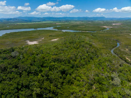 Aerial landscape by drone flight over tropical bushland and saltwater creek tributaries running from the ocean, mountains in the distance under cloudy skyの写真素材