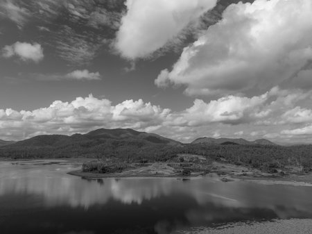 Drone aerial of a quarry on the banks of a dam filled with aquatic plants and cloud reflections on a calm day. Kinchant Dam, Australia. Monotone image.の写真素材