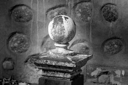 An old round concrete globe statue pitted with age, situated at the front of an abandoned stone house on the gemfields diggings Australia.の写真素材