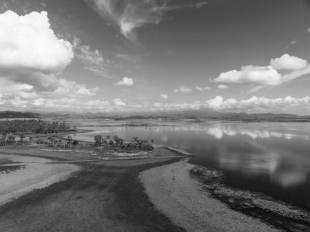 Drone aerial above a patch of land in a dam surrounded by aquatic plants and cloud reflections on...