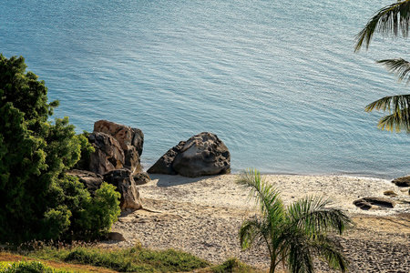 Looking down onto a small beach with palm trees and large rocks amongst the sand on the waters edge. Tropical summer day.の写真素材
