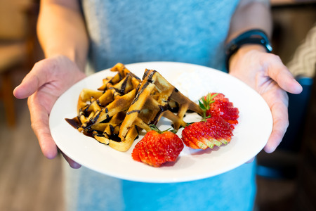 Hand holding waffles with chocolate sauce and strawberriesの写真素材