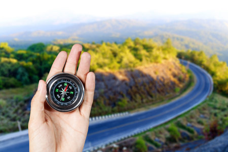 The hand of a man holding a magnetic compass over a landscape road view