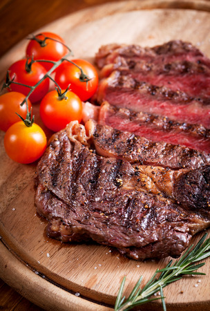 Sliced medium rare grilled Beef steak Ribeye with cherry tomatoes on cutting board, selective focusの写真素材