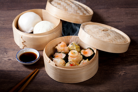 Hot Chinese Dim sum and steamed pork bun in a bamboo steamer with sauce and chopsticks on wooden table, Chinese foodの写真素材