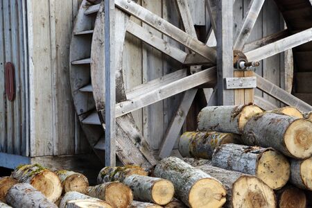 A giant wooden water wheel and cut logs next to a cabinの写真素材