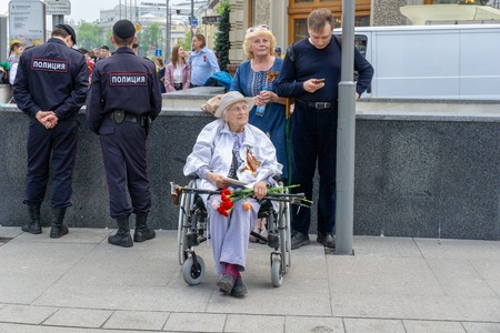MOSCOW, RUSSIA - MAY 9, 2019: Immortal regiment procession in Victory Day. Old lady sitting on a wheelchair while holding flowers in handのeditorial素材