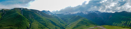 Panaromic shot of Landscape mountain view peaks in snow and green hills, deep blue sky and huge...