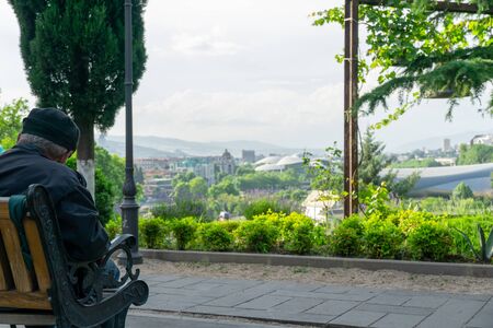 A lonely old man sitting on a bench in a park in Tbilisi among colorful summer trees.の写真素材