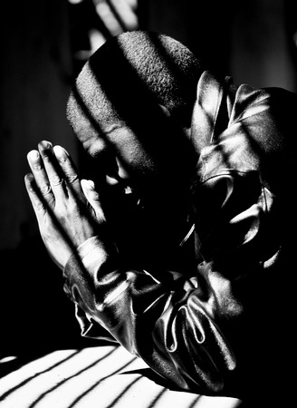 Young man praying for the safety of his country, Zimbabwe. Kneeling down, hands together.の写真素材