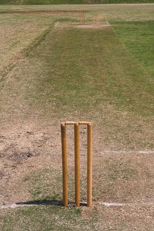a full length view of a grass cricket pitch in summer with both sets of wickets and bails setup.の写真素材